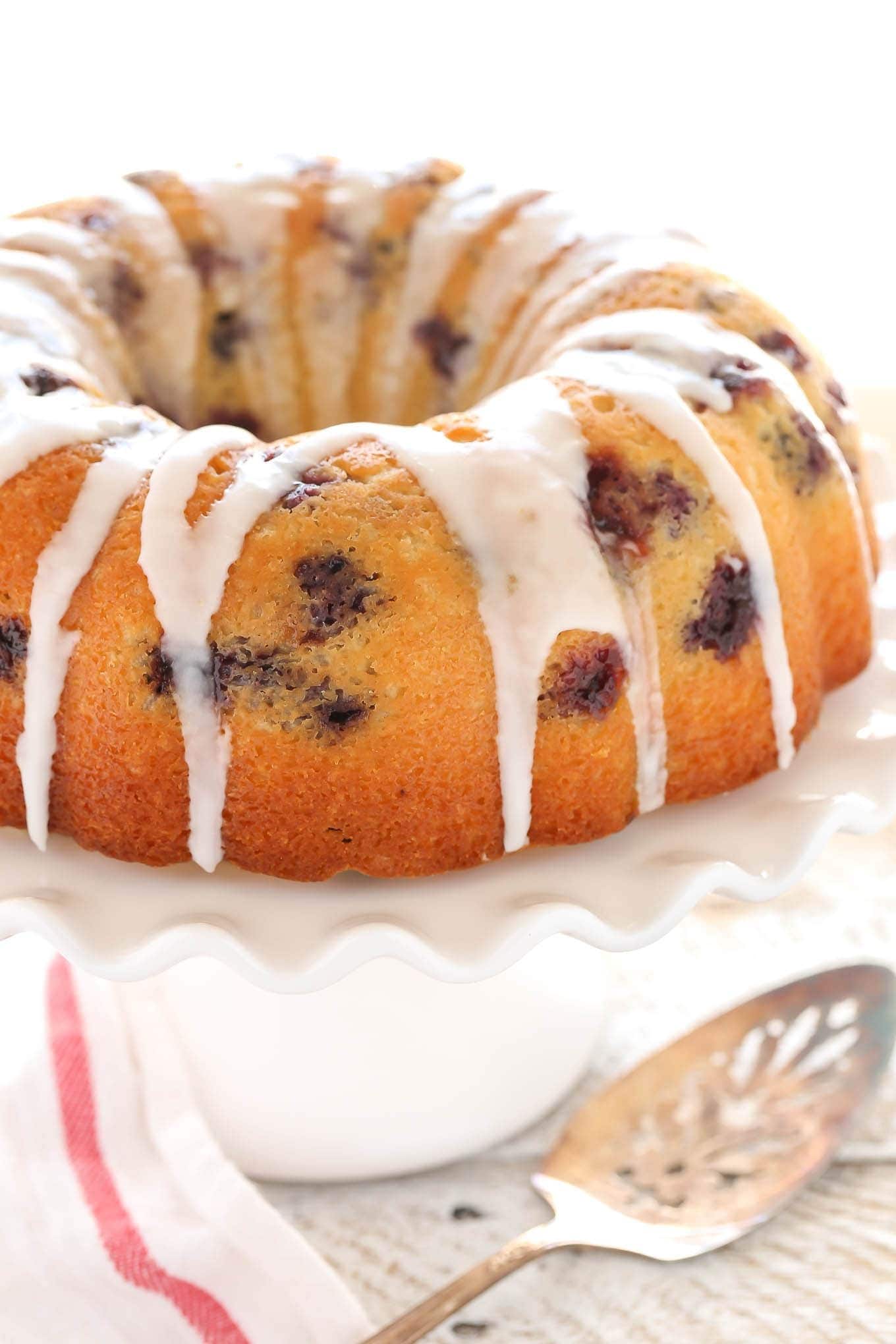 lemon-blueberry-bundt-cake-1 Bundt cake with blueberries and sugar glaze on top placed on a cake tray.