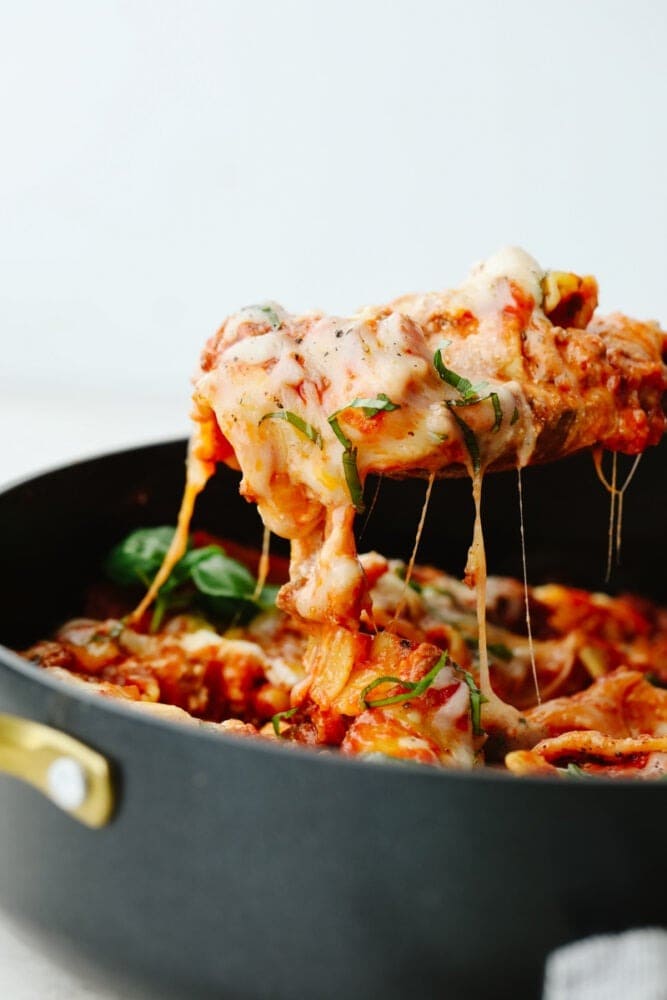 skillet-lasagna Wooden spoon scooping cheesy lasagna from a skillet.