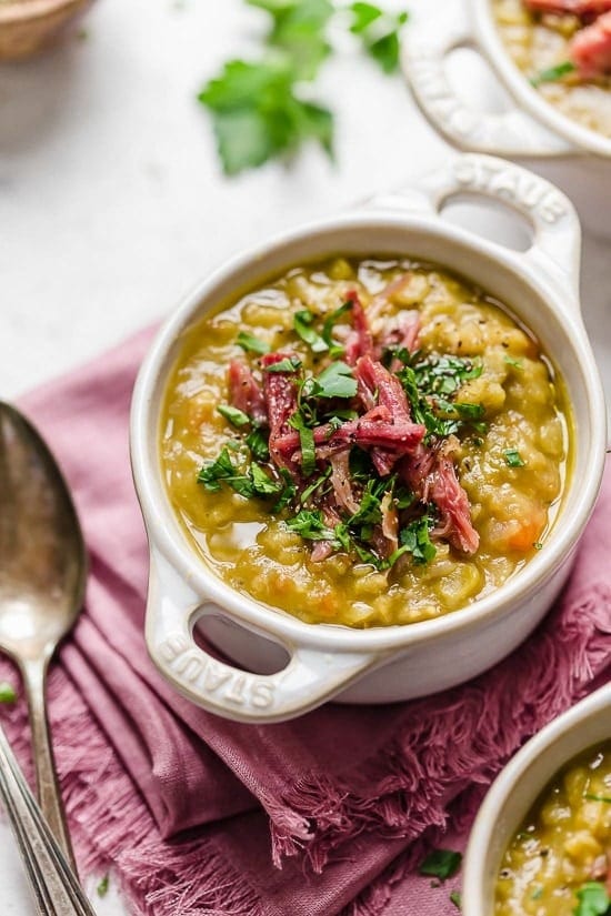 slow-cooker-split-pea-soup Split pea soup in small white ceramic pot topped with shredded meat and chopped parsley leaves.