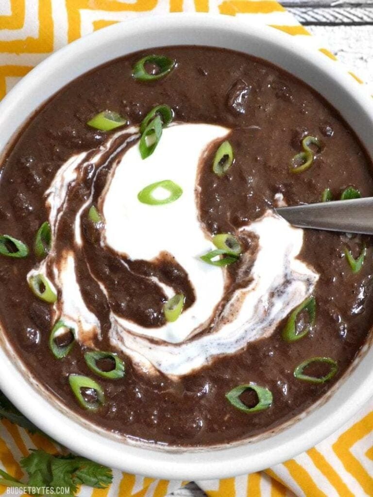 slow_cooker_black_bean_soup Black bean soup in a white bowl topped with sour cream.
