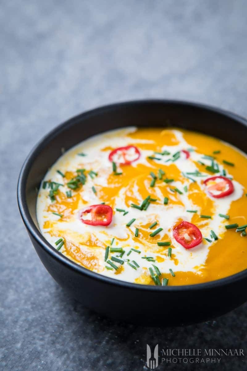 sweet-potato-soup-2 Sweet potato soup in a black bowl garnished with chives and chiles.