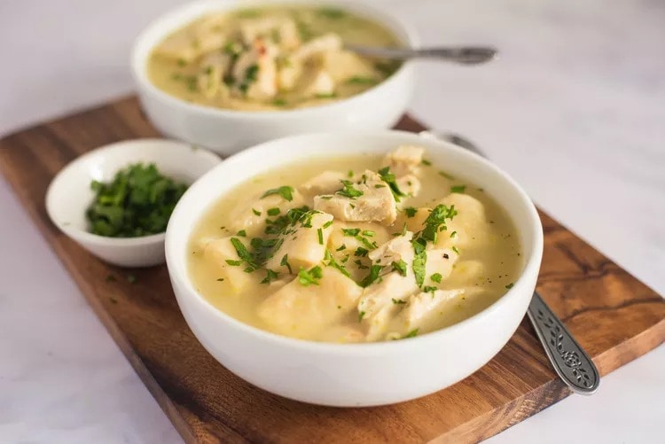 A bowl of soup with turkey meat and dumplings garnished with chopped parsley leaves served with a wooden tray.