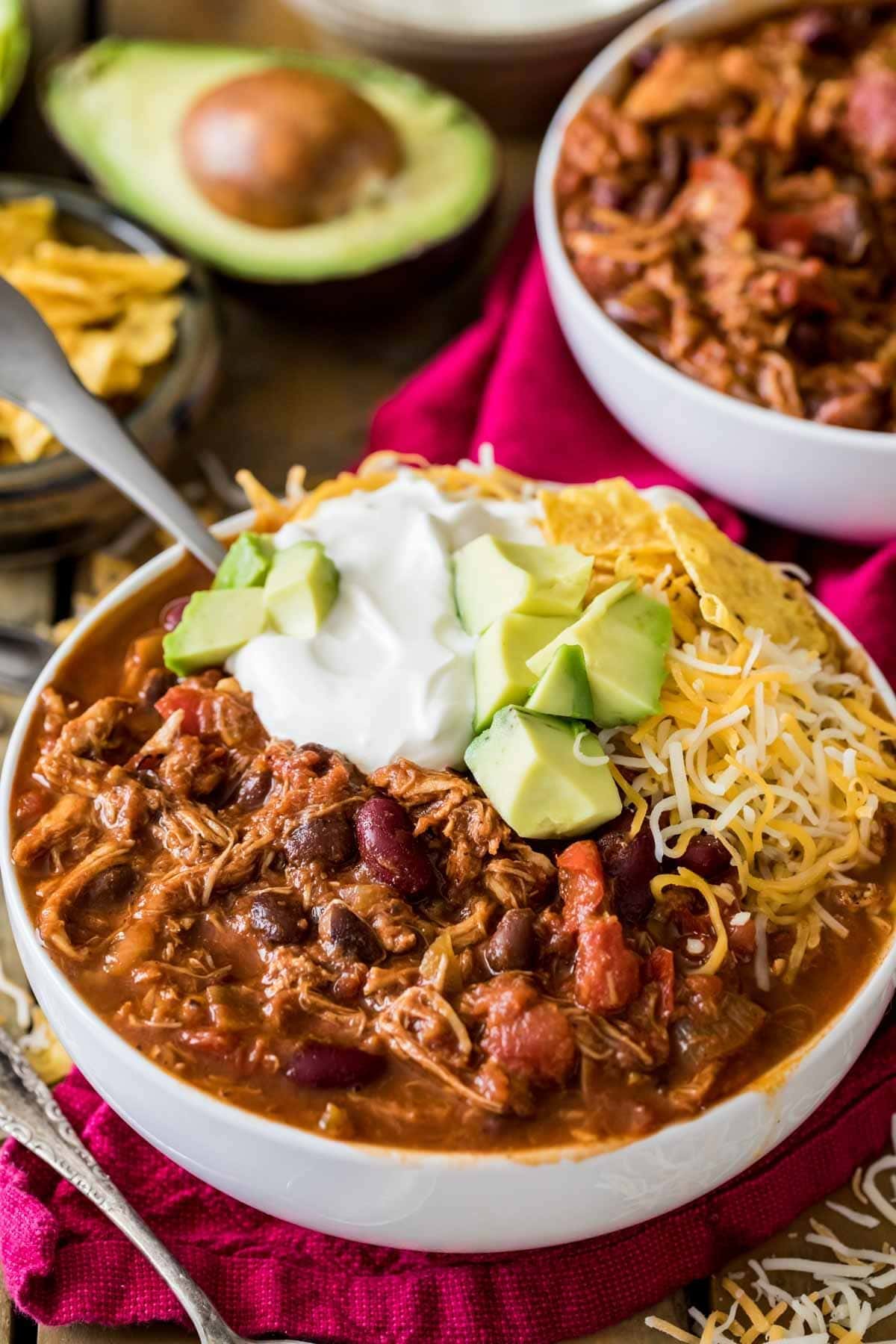 Turkey chili in a bowl topped with grated cheese, cream and avocado slices.