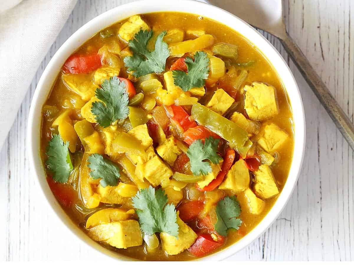 A bowl of soup made with turkey meat, flavored with curry powder, turmeric, coriander, and cinnamon mixed with onions and sliced bell peppers.