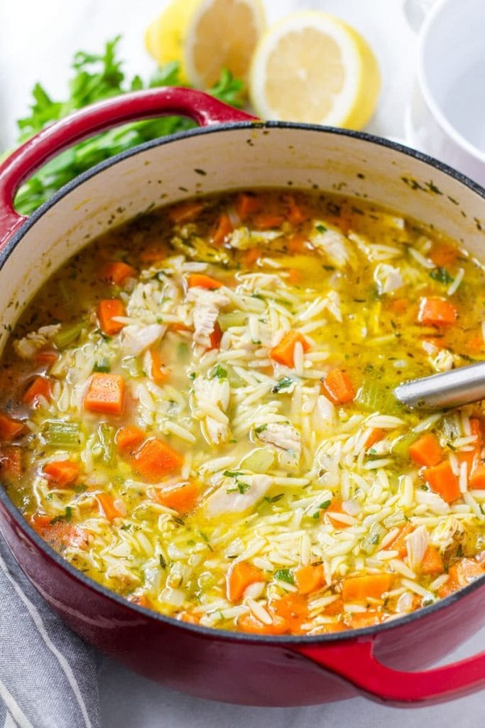 Soup on a red pot with orzo pasta and loaded with carrots and shredded turkey meat.