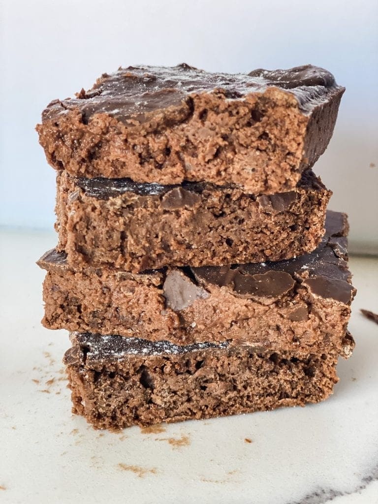 Three scrumptious fudge brownies stacked together, resting on a clean white surface.